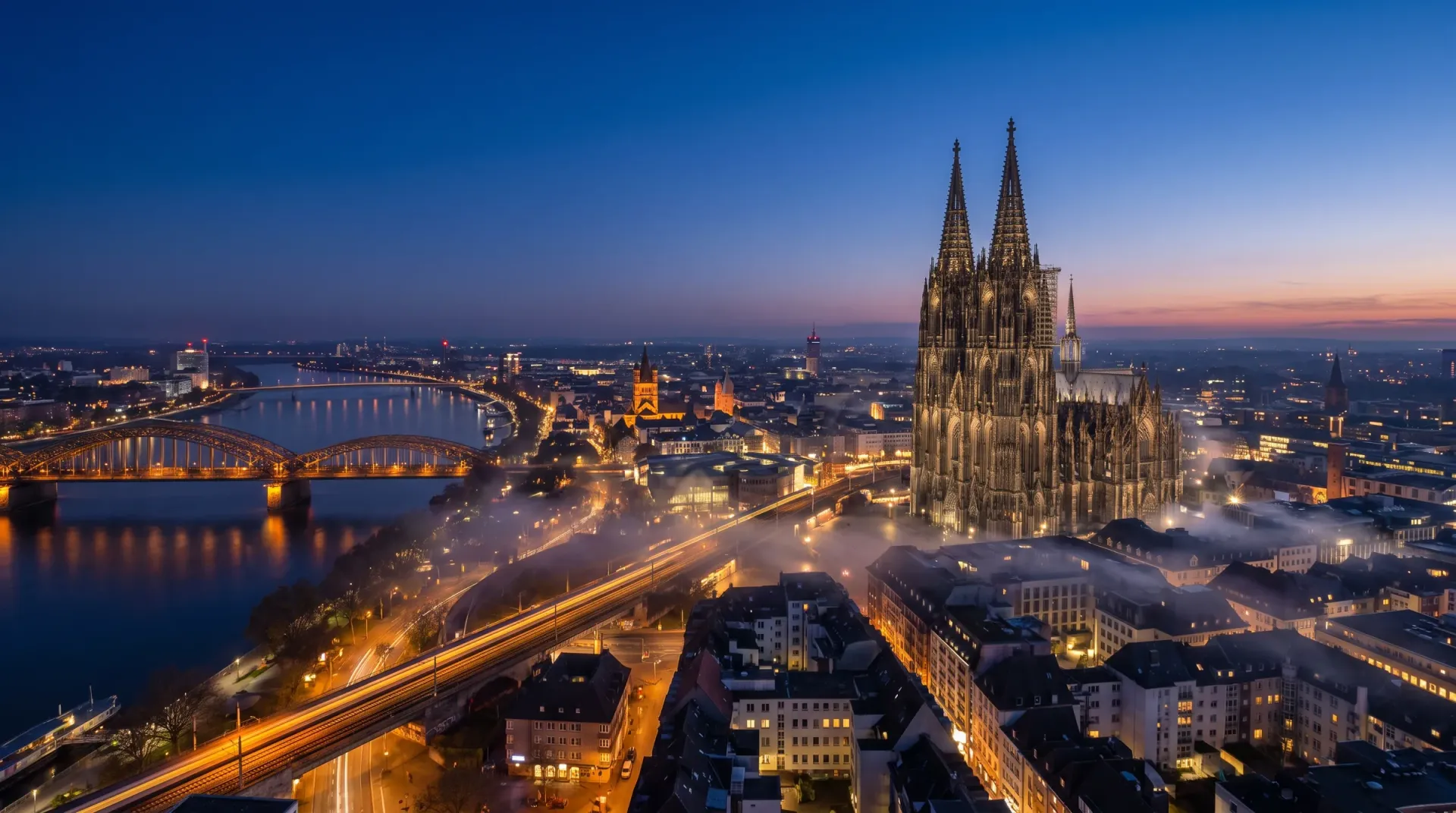 Kölner Dom und Hohenzollernbrücke zur blauen Stunde mit leuchtender Stadt